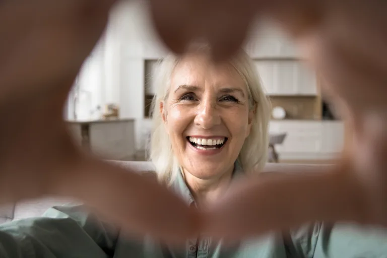 Close up face happy older woman look at camera forming heart shape with her hands, expressing love and connection through video call, highlighting warmth and affection, share tenderness and gratitude
