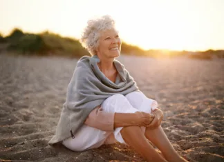 Sem edina, ki to opažam? Zakaj ima toliko žensk po 50. letu skoraj enako frizuro? Happy retired woman wearing shawl sitting relaxed on sand at the beach. Senior caucasian woman sitting on the beach outdoors
