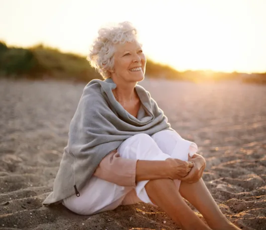 Sem edina, ki to opažam? Zakaj ima toliko žensk po 50. letu skoraj enako frizuro? Happy retired woman wearing shawl sitting relaxed on sand at the beach. Senior caucasian woman sitting on the beach outdoors