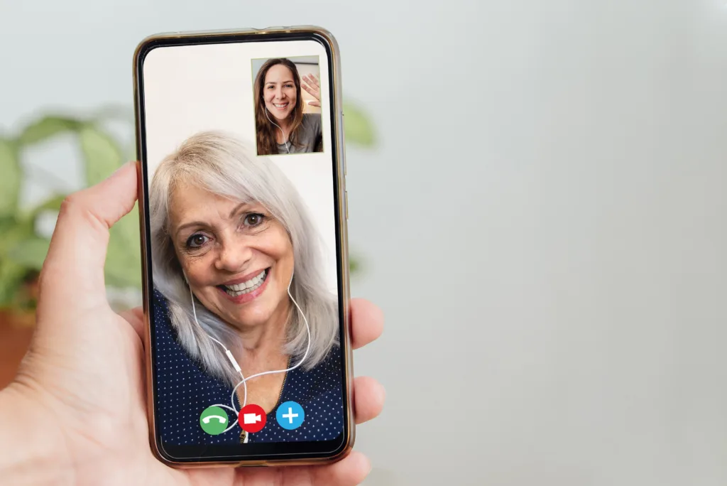 Happy senior and daughter talking on video call with mobile phone during coronavirus outbreak - Online app and social distancing concept