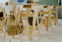 Upokojeni izkušeni pedagoški delavci, prijavite se do konca junija in pomagajte mladim Interior of classroom showing empty chairs and desks, with backpack on back of one chair, suggesting absence of students or lesson in progress