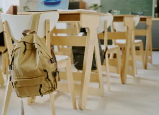 Upokojeni izkušeni pedagoški delavci, prijavite se do konca junija in pomagajte mladim Interior of classroom showing empty chairs and desks, with backpack on back of one chair, suggesting absence of students or lesson in progress
