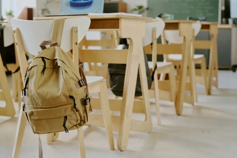 Interior of classroom showing empty chairs and desks, with backpack on back of one chair, suggesting absence of students or lesson in progress