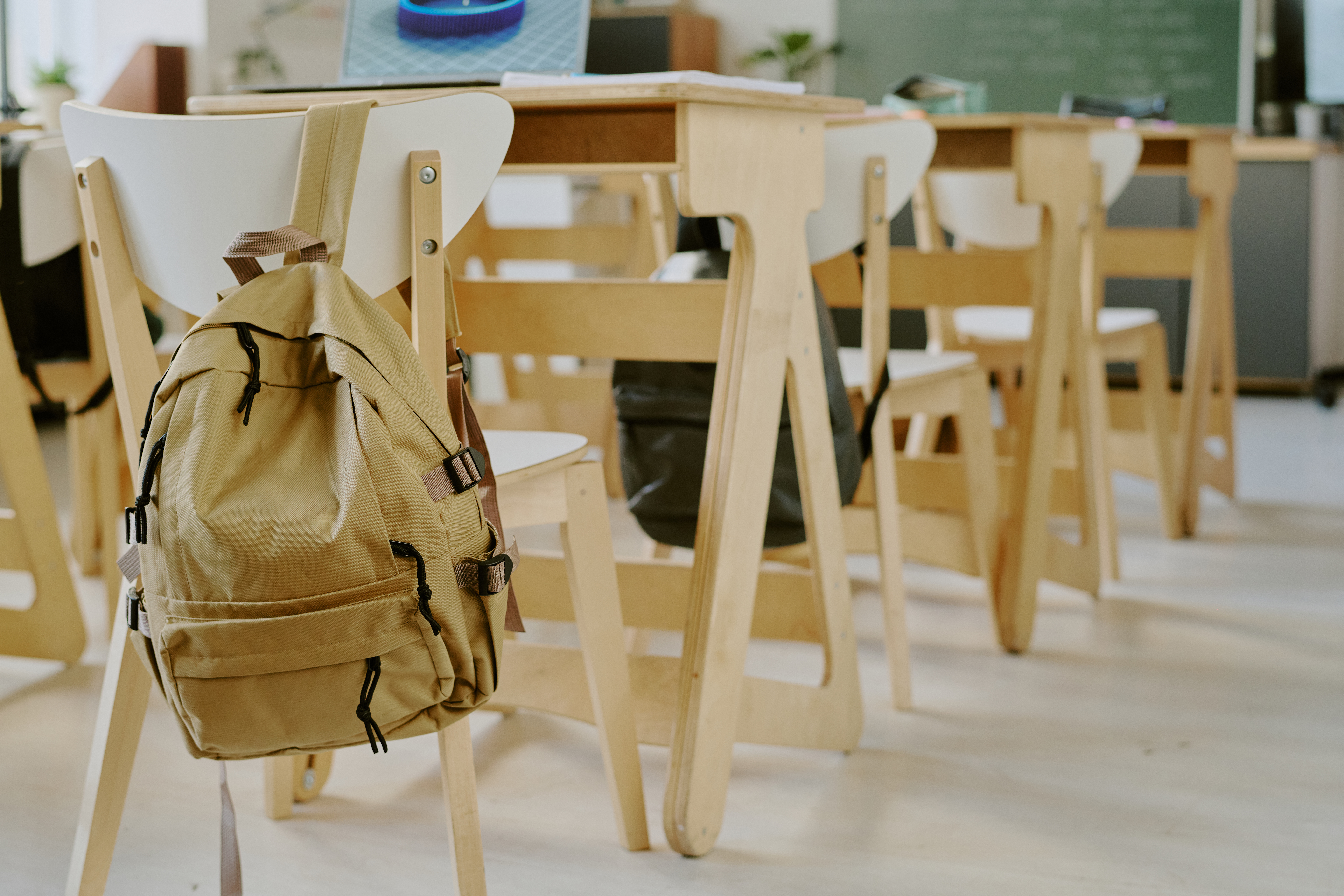 Upokojeni izkušeni pedagoški delavci, prijavite se do konca junija in pomagajte mladim Interior of classroom showing empty chairs and desks, with backpack on back of one chair, suggesting absence of students or lesson in progress