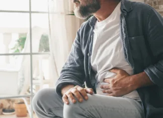 Zakaj boli trebuh? To so najpogostešji razlogi Man suffering with severe stomach pain sitting at home. Hand of mature guy holding abdomen suffering from ache, diarrhea or indigestive problem. Caucasian guy pressing on belly on painful sensation