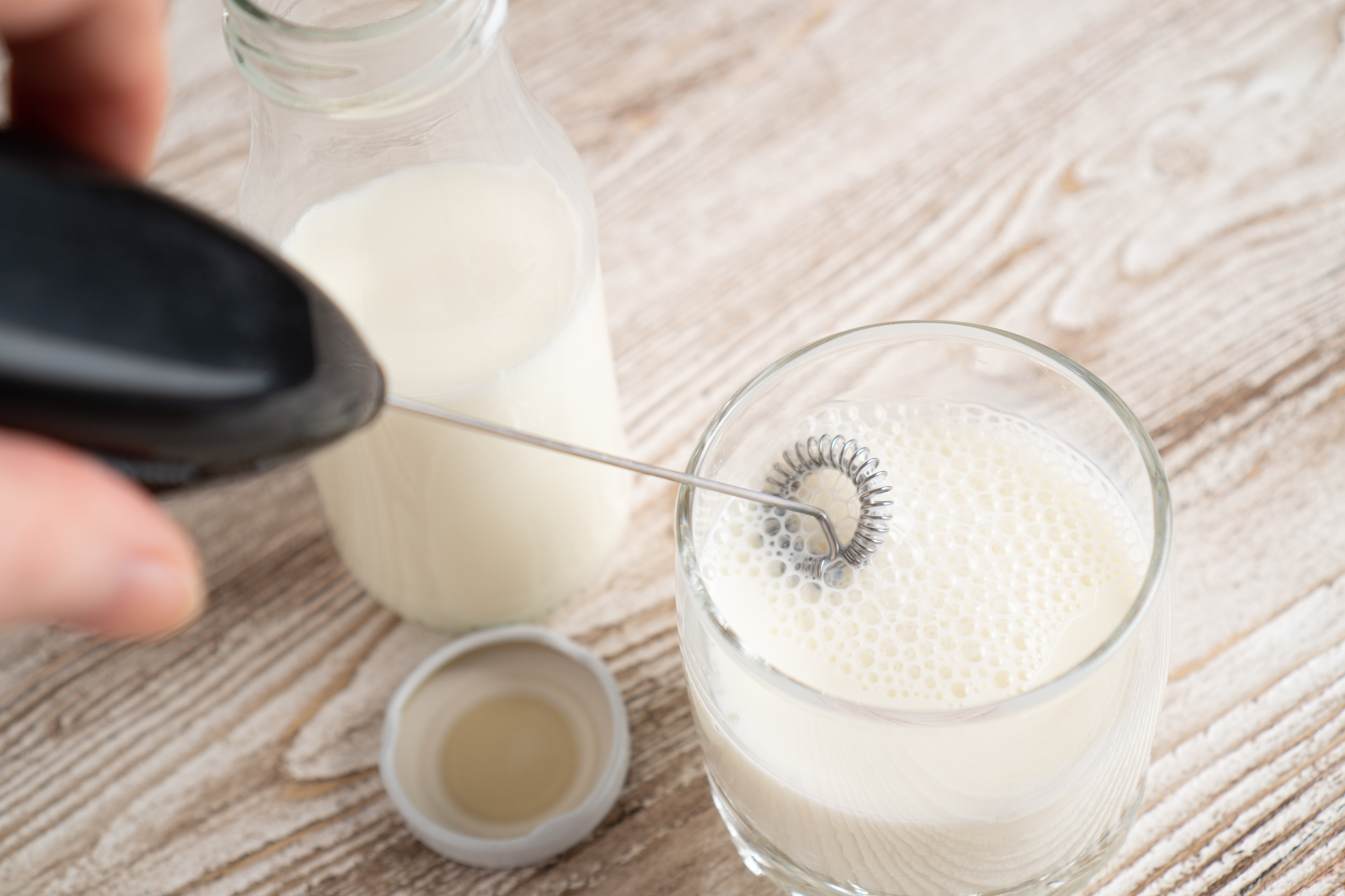 Mixing milk in glass by milk frother. Making foamy milk with frother. Milk handheld mixer. High quality photo