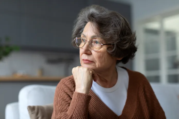 Pensive caucasian senior woman sitting on couch looking aside, thinking or pondering, feel alone lost in thoughts, mourning or yearning