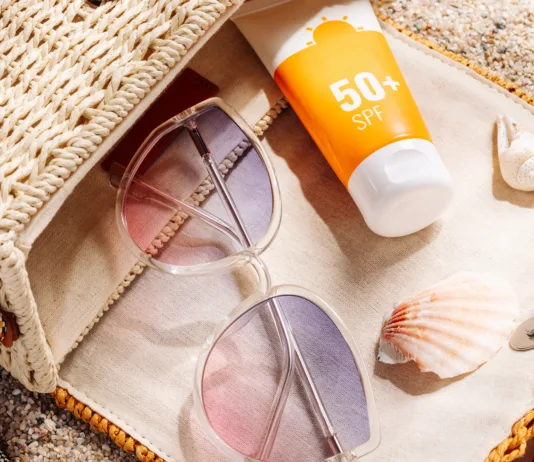 Večina dela to napako: številka na sončni kremi ne pomeni tega, kar mislite Sunscreen and glasses in a wicker straw bag on a sandy beach