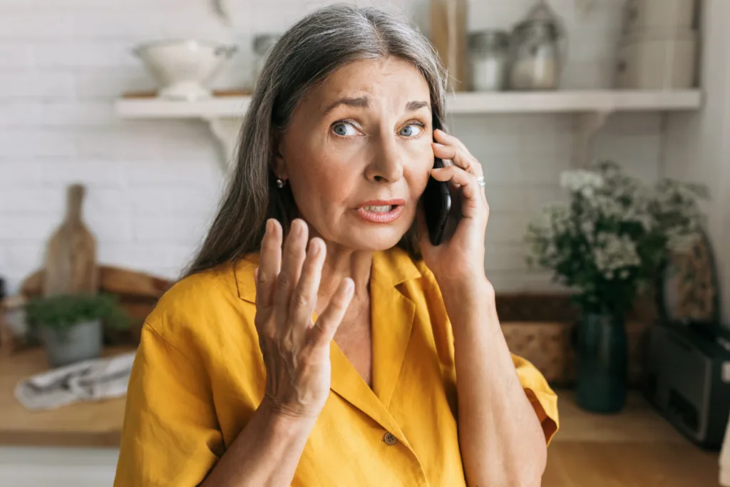 Attarctive retired female gesticulating with anxiety talking on phone, having worried face, using smartphone for conversation wih bank, trying to solve problem with savings account