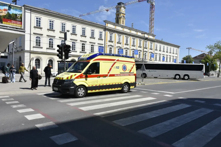 Ljubljana, Slovenia - April 27, 2026: Ljubljana Central Railway Station in Slovenia, Europe; ambulance; public transportation bus; construction site; construction crane; people walking; waiting for green light at zebra crossing; advertisement sign view; and more.