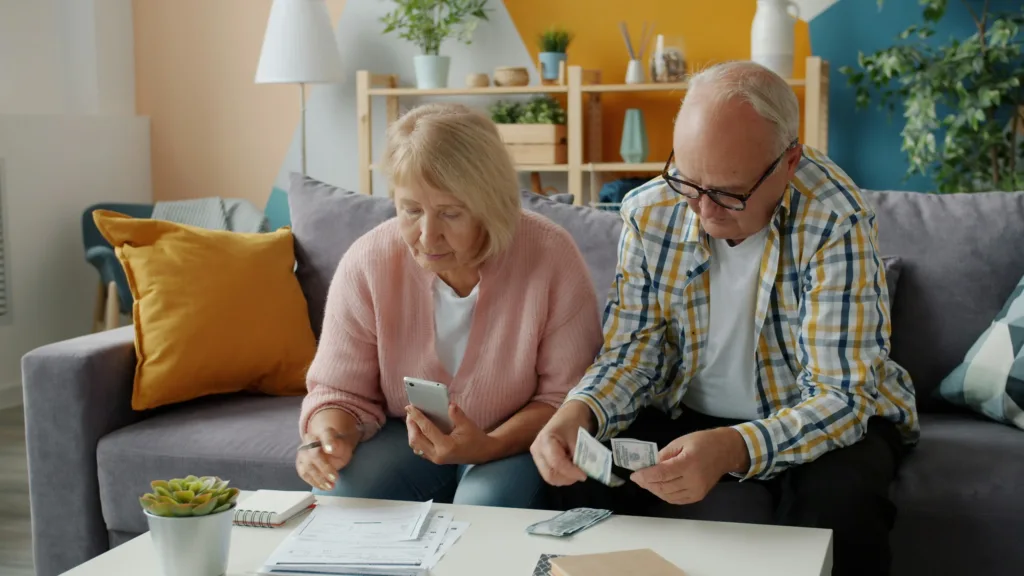 Senior couple is dealing with financial papers and counting money in apartment looking through bills together. Financial documents and cash concept.