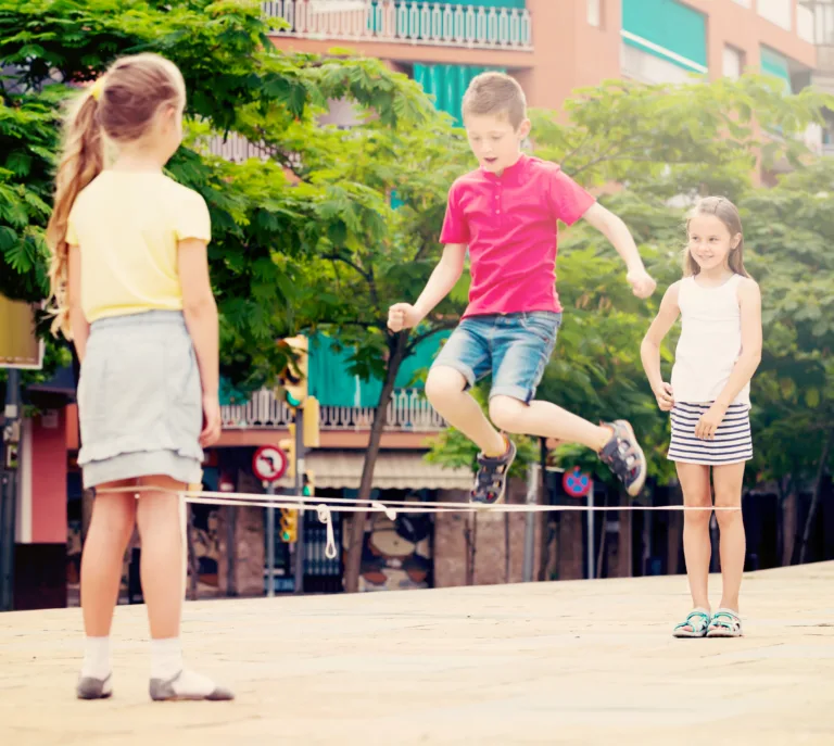 cheerful boy and girls in elementary school age playing with chinese jumping rope. Selective focus on girl