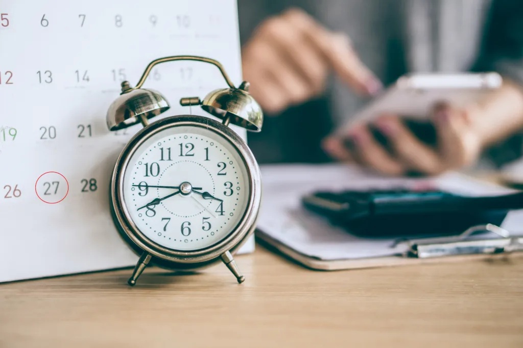 due date calendar and alarm clock with blur business woman hand calculating monthly expenses during tax season.