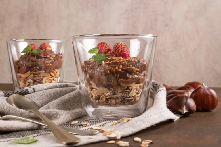 Glass cups of chocolate and chestnuts mousse with roasted almonds and oats decorated with raspberry and mint leaves.