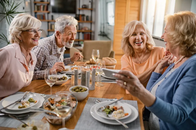 Happy mature friends having lunch together and taking selfie with mobile phone at dining table.