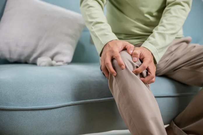 Old age. Asian senior man retirement knee joint pain on sofa, Elderly old man sitting down hands hold knee, Grandfather people health care bone problem at home
