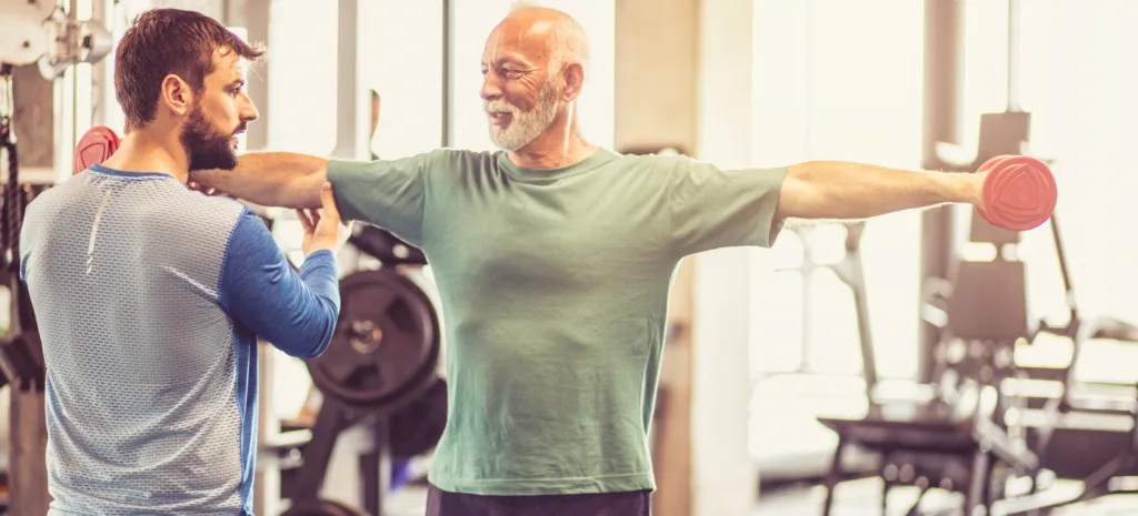 Practice with lots of strength. Fitness instructor helping senior man in exercise.