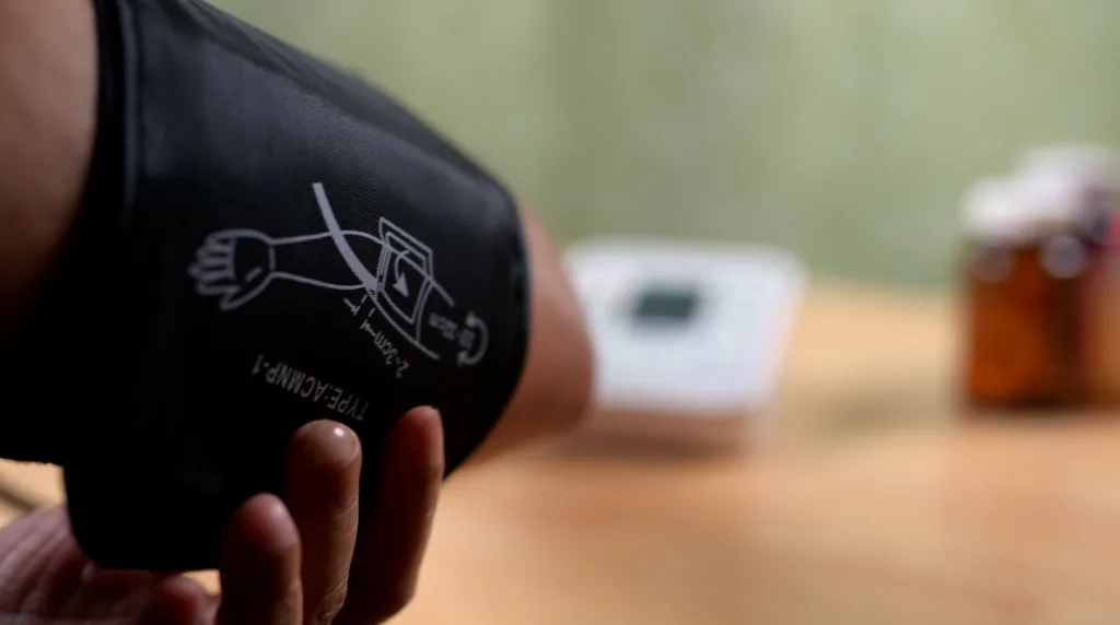Unrecognizable person monitors cardiovascular health by checking blood pressure inside domestic kitchen setting, promoting wellness, preventive healthcare, self-care, and daily routine.